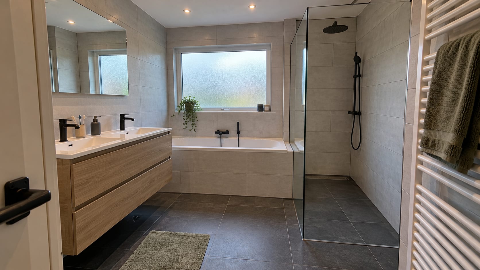 Opgeleverde badkamer in Zevenbergen: een ligbad met betegelde ombouw, een inloopdouche met glazen wand en douchegoot, en een eiken badmeubel.