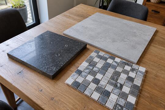 Tegelvoorbeelden op tafel: mozaïek op gaas, hardsteen en een groot formaat tegel.