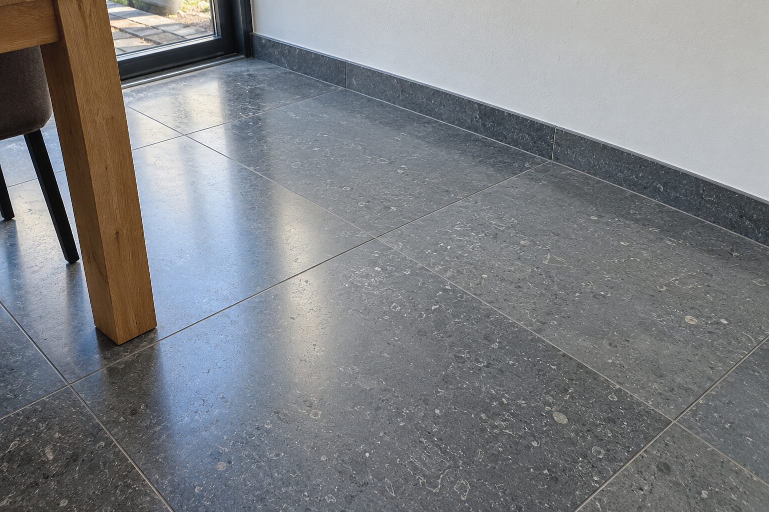 Strak gelegde vloer van grijze natuursteen in een eetkamer, netjes afgewerkt met een plint.