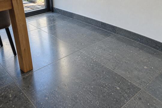 Vloer van grijze natuursteen rond de eethoek, netjes afgewerkt met plinten.