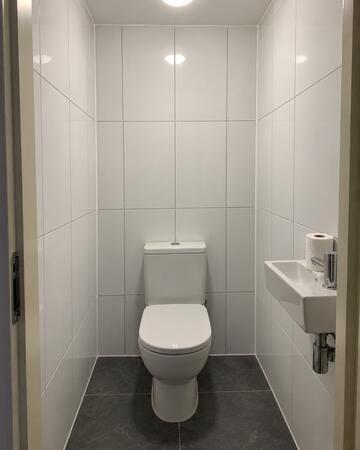 Modern toilet met glanzende witte wandtegels tot het plafond en donkere vloertegels.
